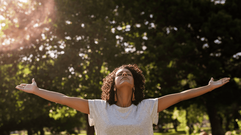 Person i naturen med armarna utsträckta i ett ögonblick av lugn och medveten närvaro, som symbol för mindfulness vid långvarig smärta.